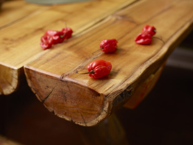 Close Up of Whole Raw Red Scotch Bonnet Peppers on a Wooden Table with Bokeh Effects