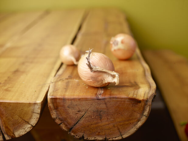 Whole Fresh Yellow Onion Bulbs on Wooden Table with Green Background and Bokeh Effect