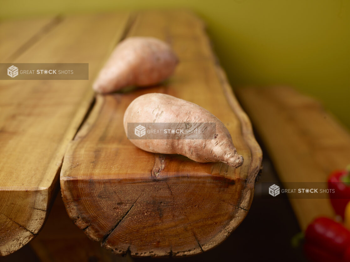 Whole Raw Sweet Potatoes on Wooden Log Table with Green Background and Bokeh Effect