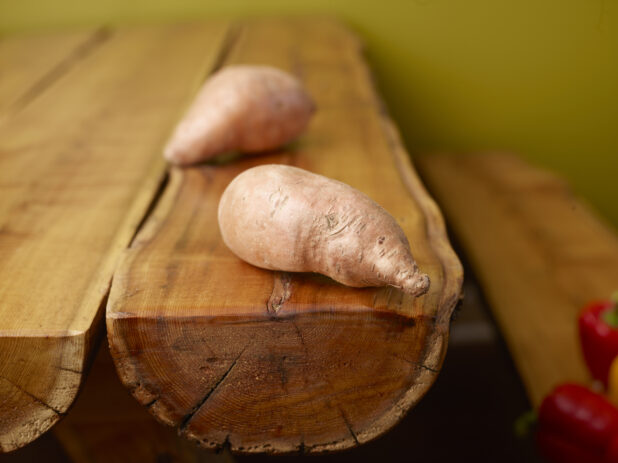Whole Raw Sweet Potatoes on Wooden Log Table with Green Background and Bokeh Effect
