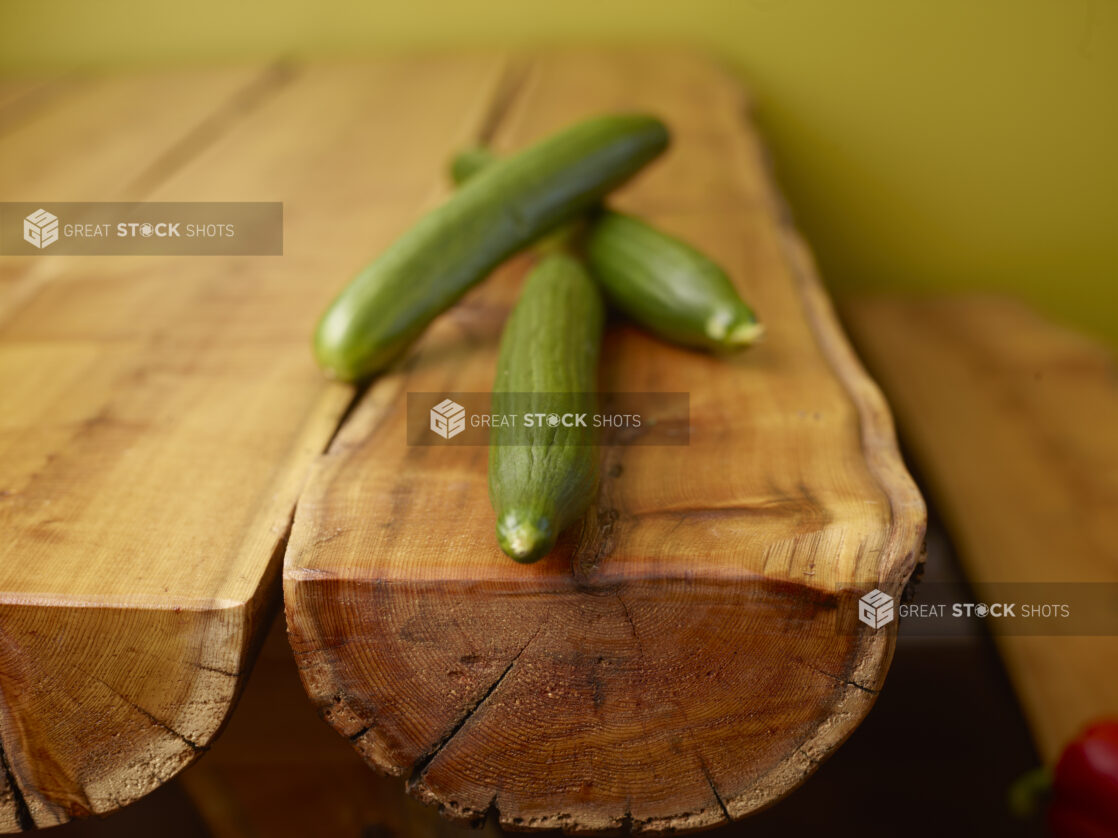 Fresh Whole Cucumbers on Wooden Log Table with Green Background and Bokeh Effect