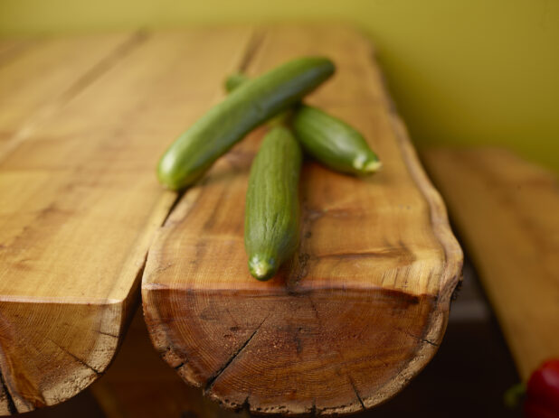 Fresh Whole Cucumbers on Wooden Log Table with Green Background and Bokeh Effect