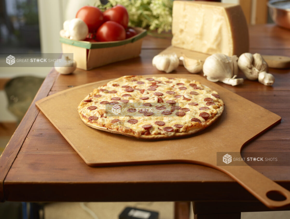 Whole Pepperoni Pizza on a Wooden Pizza Peel, Surrounded by Fresh Pizza Ingredients on a Wooden Table in a Restaurant Interior