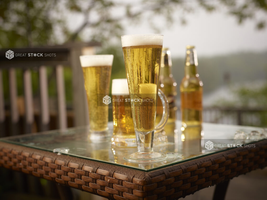 Half Pint of Draught Beer with Assorted Sized Glasses and Bottles of Beer on a Patio Table in an Outdoor Setting