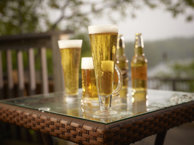 Half Pint of Draught Beer with Assorted Sized Glasses and Bottles of Beer on a Patio Table in an Outdoor Setting