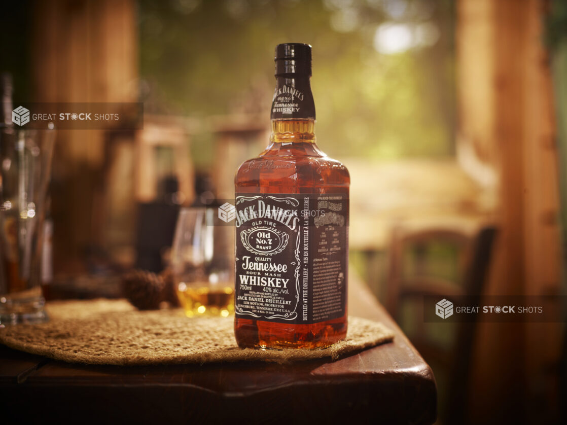 750ml Bottle of Jack Daniels Tennessee Whiskey on a Woven Placemat and Wooden Table in an Indoor Setting with Moody Lighting