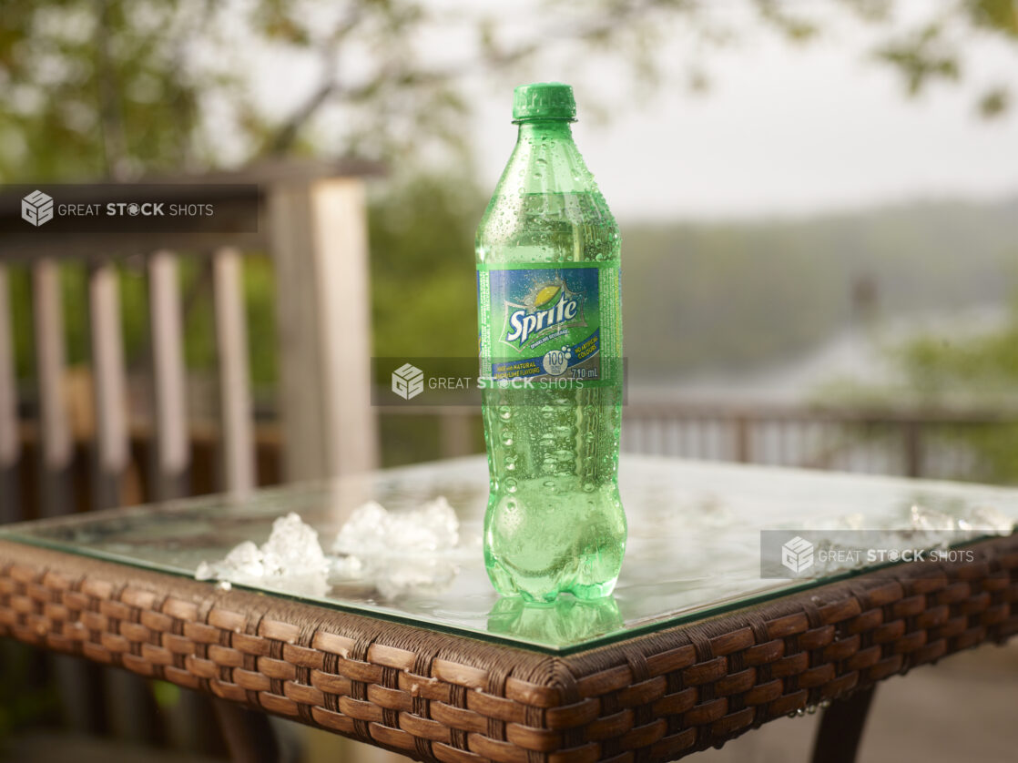 Plastic Bottle of Coca-Cola Brand Sprite Soft Drink on a Glass Patio Table with Ice Cubes in an Outdoor Setting