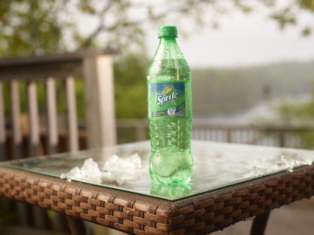 Plastic Bottle of Coca-Cola Brand Sprite Soft Drink on a Glass Patio Table with Ice Cubes in an Outdoor Setting