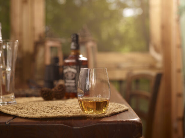 Stemless Glassware with Two Fingers of Jack Daniels Whiskey Neat on a Woven Placemat and Wooden Table in an Indoor Setting