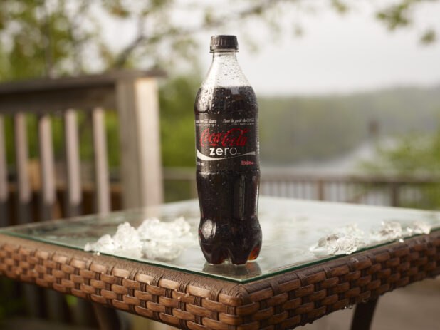Plastic Bottle of Coca-Cola Brand Coke Zero Soft Drink on a Glass Patio Table with Ice Cubes in an Outdoor Setting