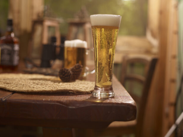 Close Up of a Pilsner Glass of Draught Beer on a Woven Placemat and Wooden Table in an Indoor Setting