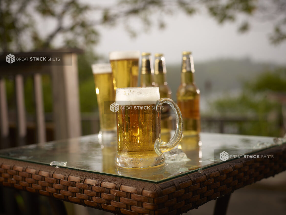 Glass Stein of Draught Beer with Assorted Sized Glasses and Bottles of Beer on a Patio Table in an Outdoor Setting