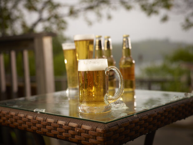 Glass Stein of Draught Beer with Assorted Sized Glasses and Bottles of Beer on a Patio Table in an Outdoor Setting
