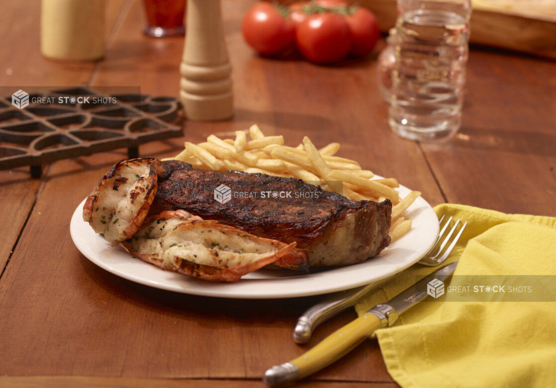 Surf and Turf Dinner Plate with Steak, Lobster Tails and French Fries on a Restaurant Table Setting - variation