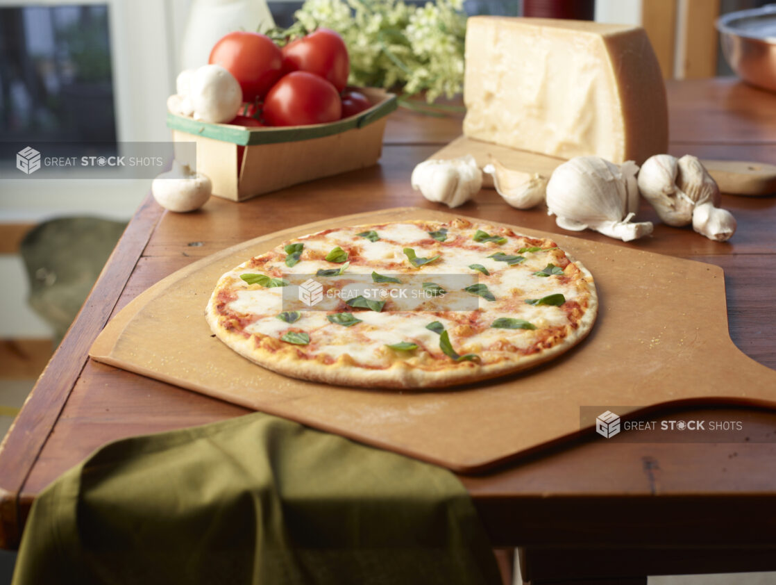 Whole Margherita Pizza on a Wooden Pizza Peel, Surrounded by Fresh Pizza Ingredients on a Wooden Table in a Restaurant Interior