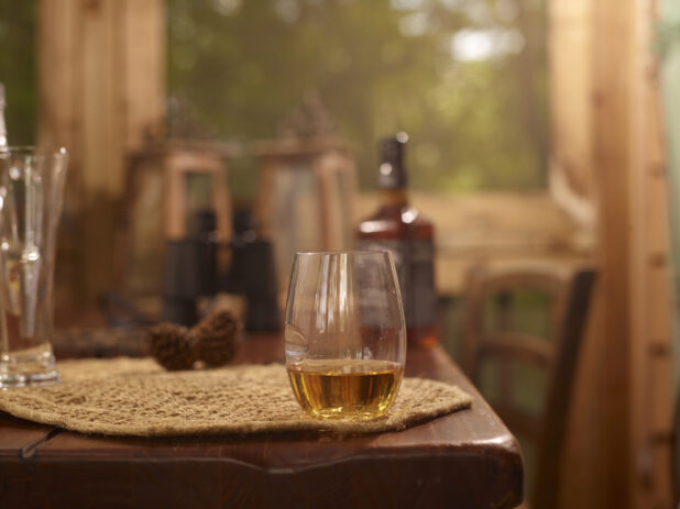 Stemless Glassware with Two Fingers of Jack Daniels Whiskey Neat on a Woven Placemat and Wooden Table in an Indoor Setting - Variation