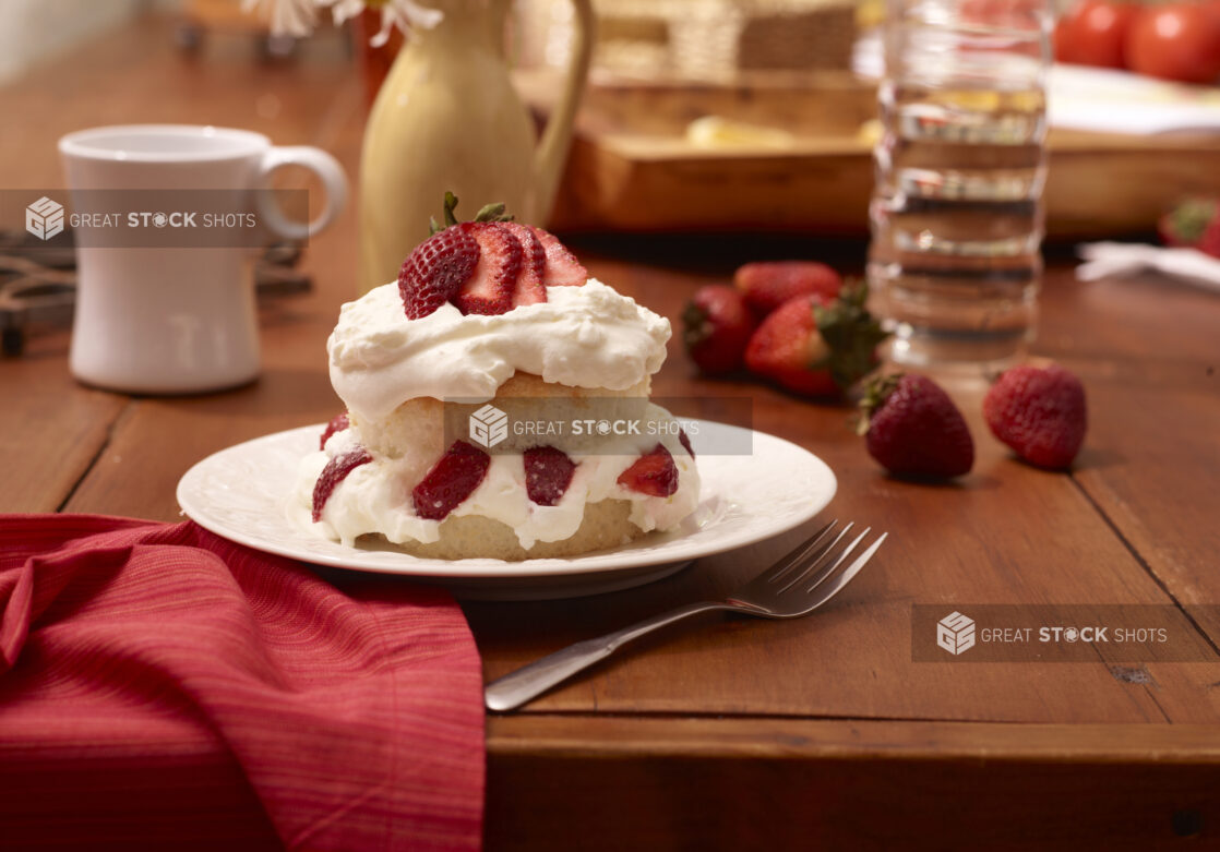 Strawberry Shortcake with Fresh Strawberries and Whipped Cream on a White Ceramic Dish on a Wooden Table in an Indoor Setting