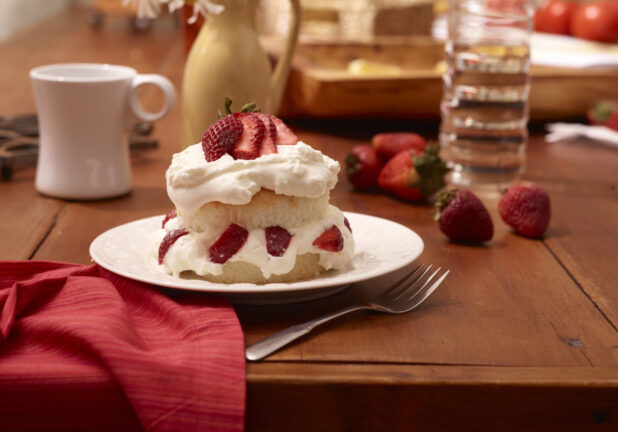 Strawberry Shortcake with Fresh Strawberries and Whipped Cream on a White Ceramic Dish on a Wooden Table in an Indoor Setting