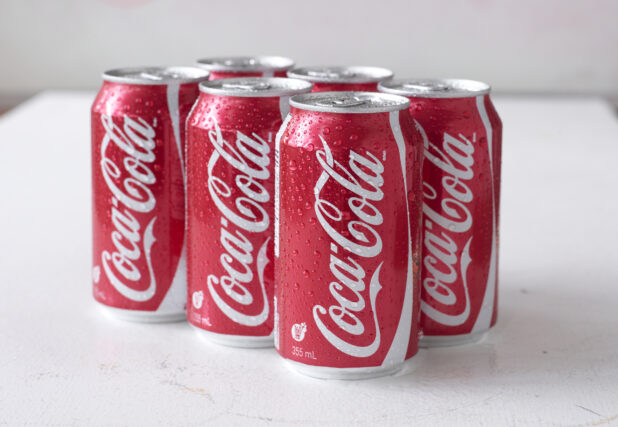 6-Pack of Coca-Cola Soft Drink Cans on a White Surface in an Indoor Setting