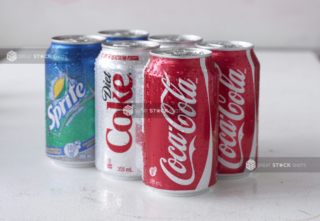 6-Pack of Assorted Coca-Cola Beverage Soft Drink Cans on a White Surface in an Indoor Setting