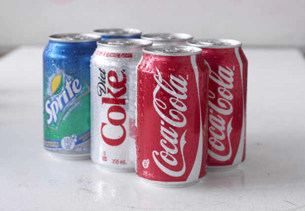6-Pack of Assorted Coca-Cola Beverage Soft Drink Cans on a White Surface in an Indoor Setting
