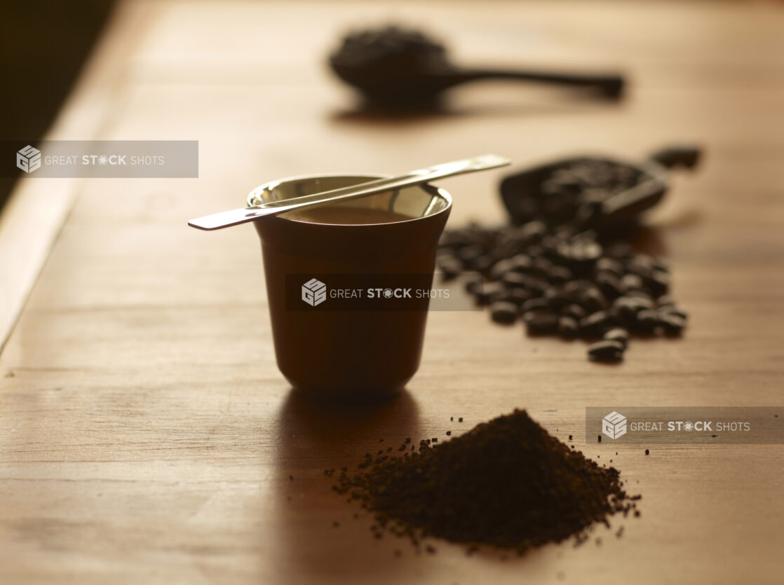 Coffee in a Stainless Steel Asian Tea Cup on a Wooden Surface with Coffee Beans and Ground Coffee in an Indoor Setting