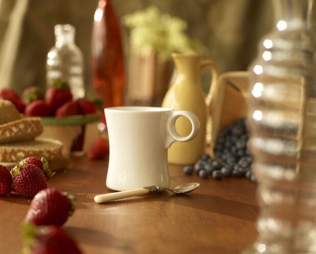White Ceramic Coffee Mug Surrounded by Fresh Blueberries, Strawberries and Bread on a Wooden Table in an Indoor Setting
