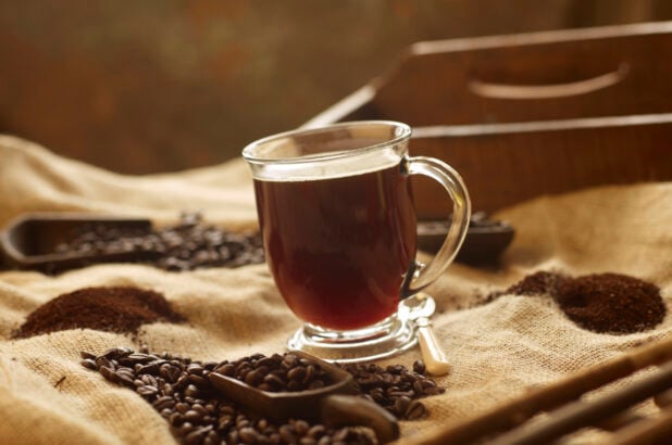 Black Coffee in a Glass Mug on a Burlap Material Surface with Coffee Beans and Ground Coffee in an Indoor Setting