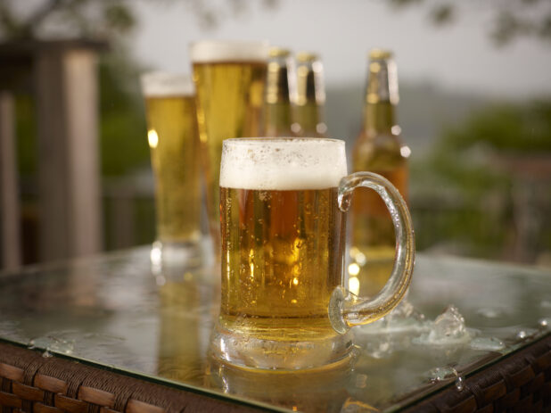 Close Up of Glass Stein of Draught Beer with Assorted Sized Glasses and Bottles of Beer on a Patio Table in an Outdoor Setting