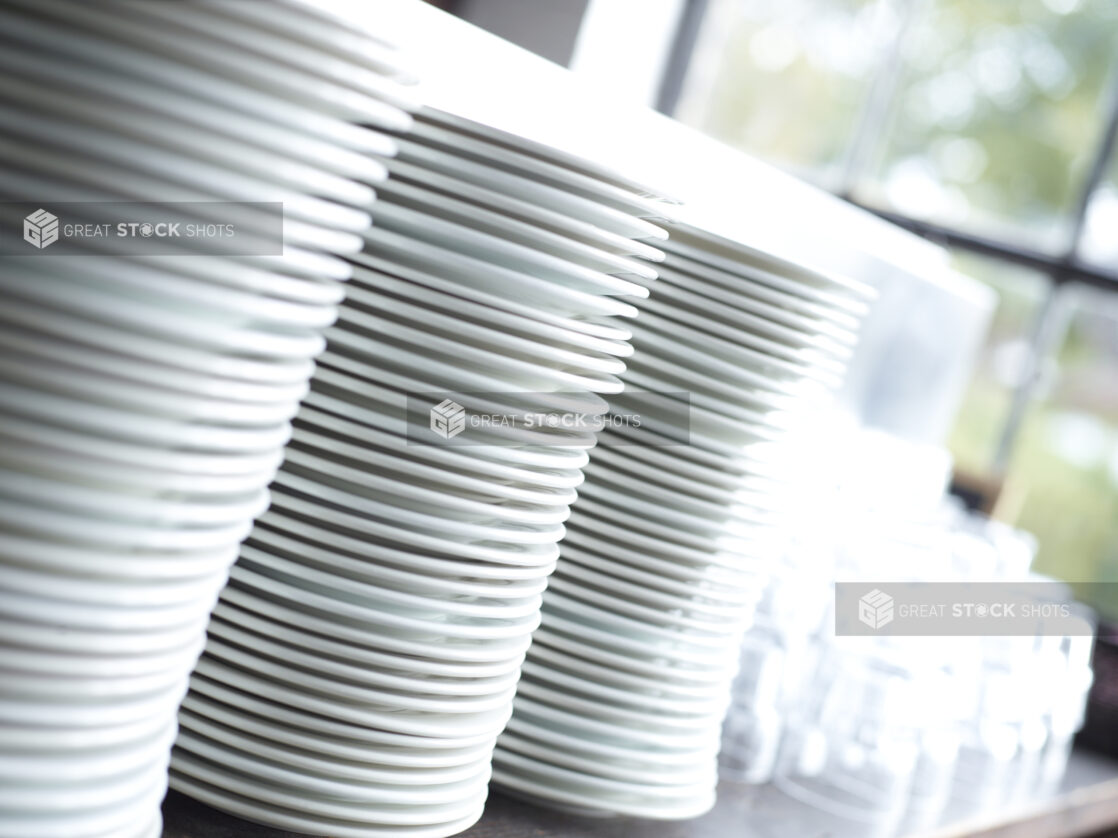 Clean Stacks of White Dinner Plates and Water Glasses with Bokeh Effect