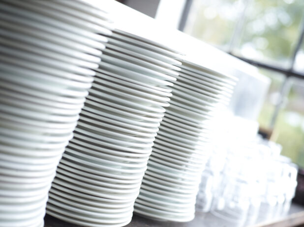 Clean Stacks of White Dinner Plates and Water Glasses with Bokeh Effect