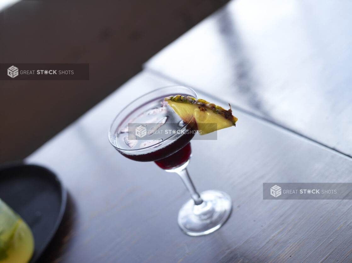 Cocktail in Daiquiri Glass with Pineapple Wedge Garnish on a Dark Wooden Table Surface