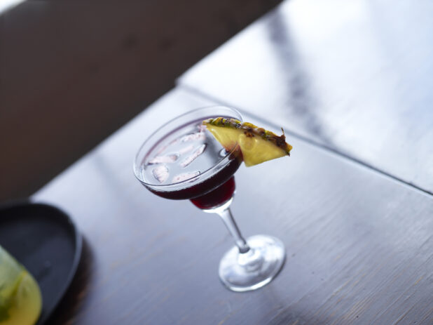 Cocktail in Daiquiri Glass with Pineapple Wedge Garnish on a Dark Wooden Table Surface