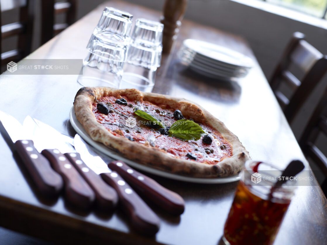 Neapolitan-Style Pizza with Black Olives on Restaurant Table setting with cutlery, dishes and glasses