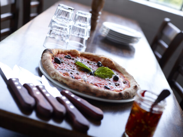 Neapolitan-Style Pizza with Black Olives on Restaurant Table setting with cutlery, dishes and glasses
