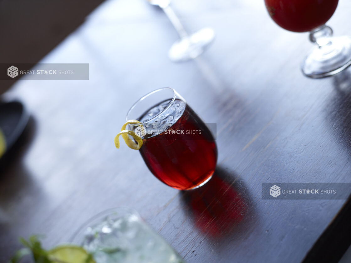 Cocktail with Citrus Peel Twist Garnish on Dark Wooden Table with Other Assorted Drinks