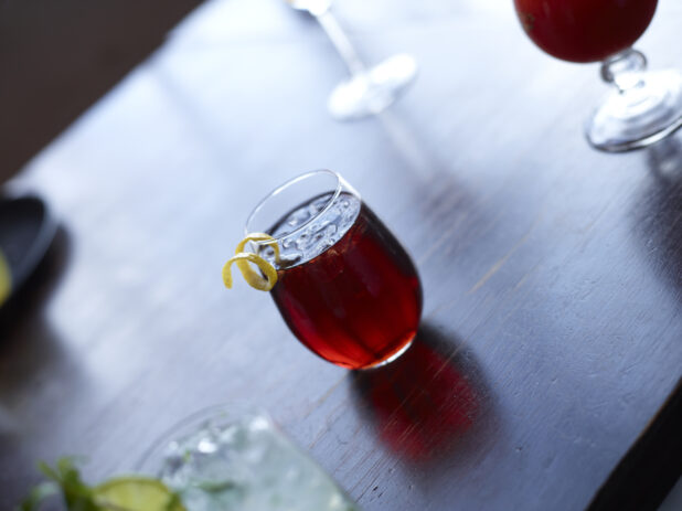 Cocktail with Citrus Peel Twist Garnish on Dark Wooden Table with Other Assorted Drinks