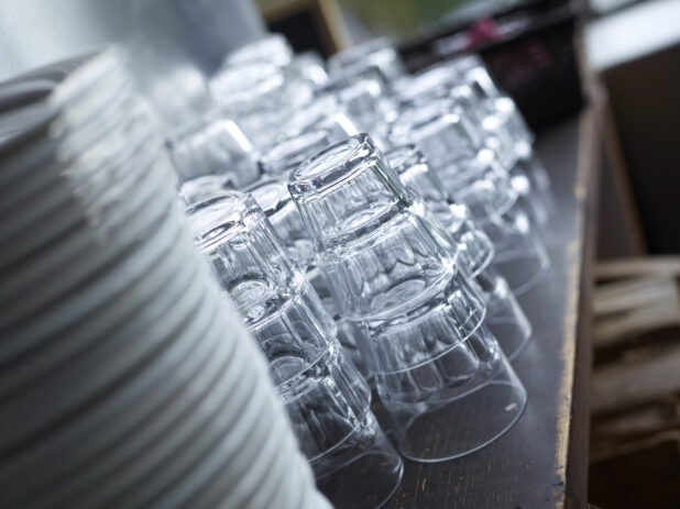 Clean Stacks of Water Glasses and White Dinner Plates with Bokeh Effect