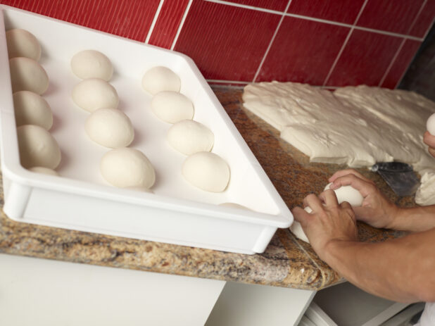 A person shaping pizza dough on a prep station