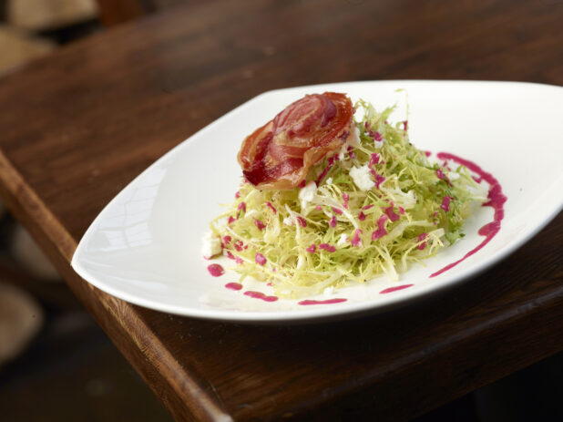 Frisée Salad with Bacon, Feta Cheese and Raspberry Dressing on White Plate in Restaurant Setting