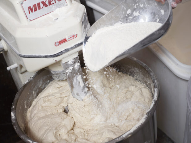 Person Adding Flour to Pizza Dough Mixing Machine