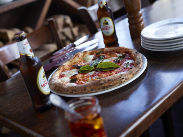 Neapolitan-Style Margherita Pizza with Italian Beer in Bottles on Restaurant Table Setting