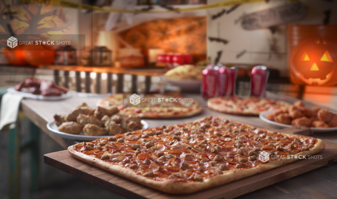 Halloween Pizza Party with Assorted Large Pizzas, Chicken Wings, Cans of Soda and Decorations in an Indoor Setting