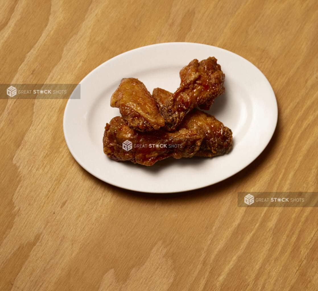 Jumbo Sauced Chicken Wings on a Round White Plate, Close Up on a Wooden Surface