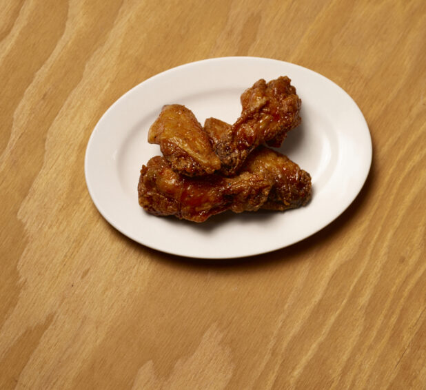 Jumbo Sauced Chicken Wings on a Round White Plate, Close Up on a Wooden Surface