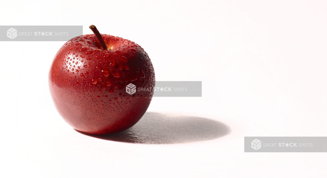 A red apple with beads of water on a white background