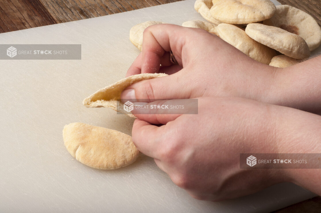 Hands opening a mini pita on a white cutting board on a rustic wooden table