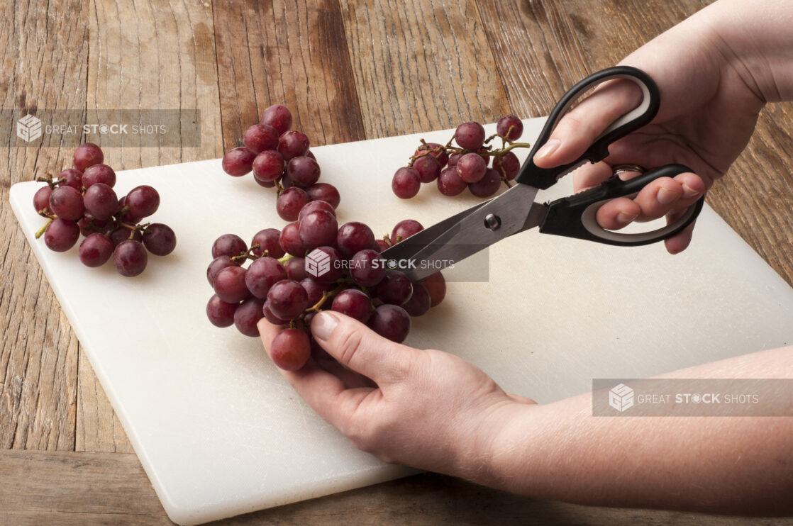 Hands cutting grapes over a white cutting board on a rustic wooden table