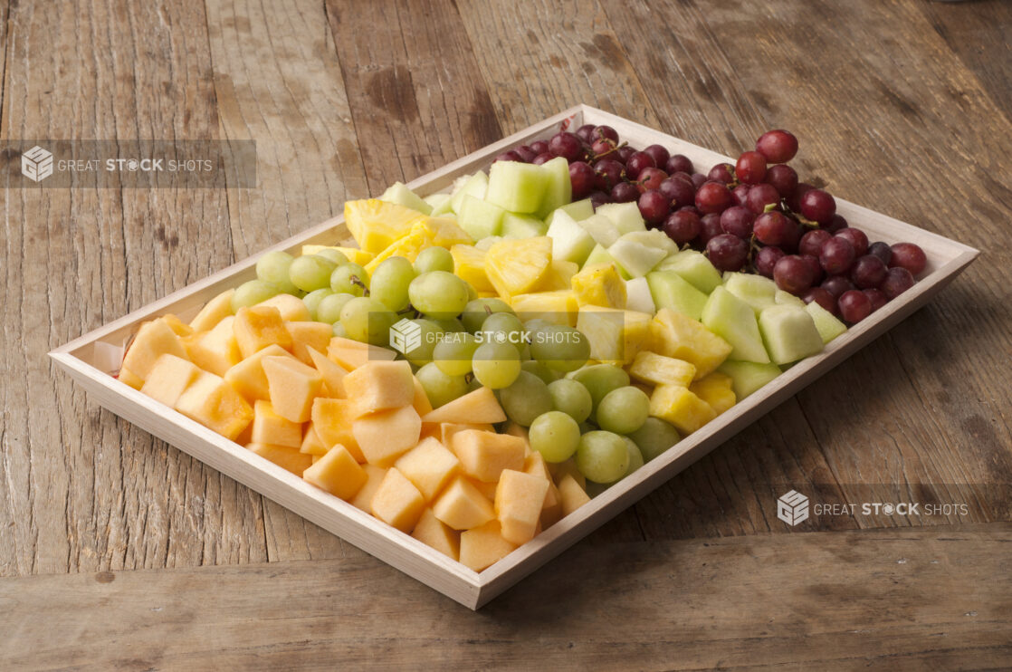 Fruit platter on a wooden tray on a rustic wooden table, close-up