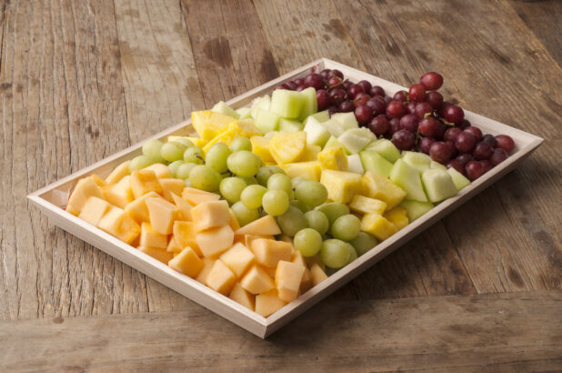 Fruit platter on a wooden tray on a rustic wooden table, close-up